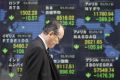 Man walks past an electronic board displaying falls in market indices from around the world outside a brokerage in Tokyo