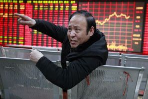An investor gestures as he talks to a person in front of an electrical board showing stock information at a brokerage house in Huaibei