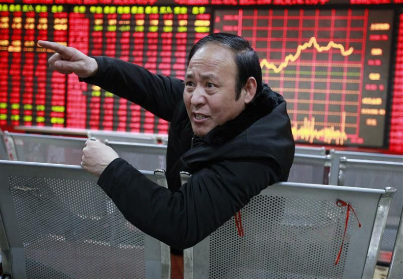 An investor gestures as he talks to a person in front of an electrical board showing stock information at a brokerage house in Huaibei