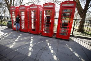 A tourist poses for a photo next to four telephone boxes next to Hyde Park, in central London