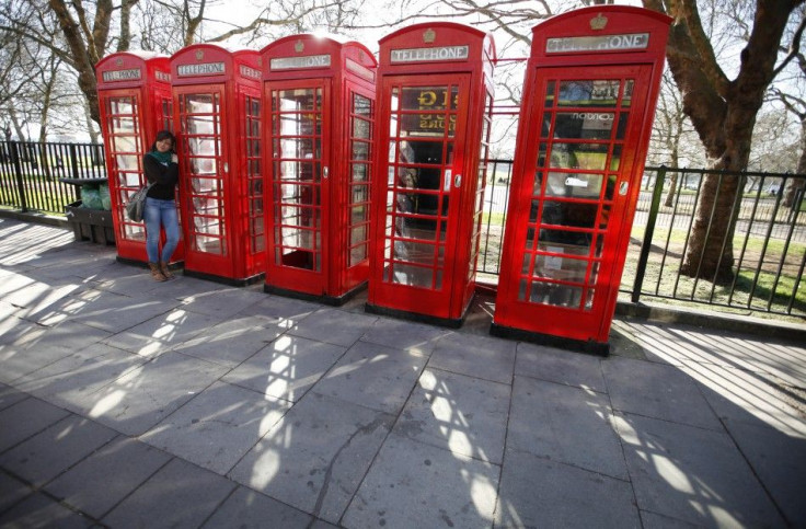 A tourist poses for a photo next to four telephone boxes next to Hyde Park, in central London