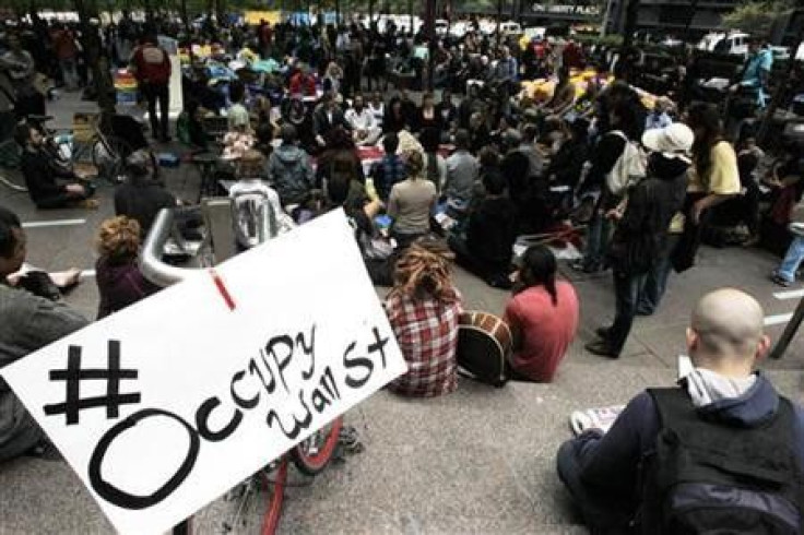 Occupy Wall Street protesters meditate while a sign bearing their twitter handle hangs from a railing in Zuccotti Park in New York