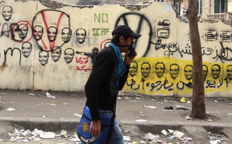 A young man wearing a mask to protect him from tear gas passes a wall with graffiti of Chairman of the ruling Supreme Council of the Armed Forces SCAF Mohamed Hussein Tantawi, in the shadow of clashes between police and protesters near the Interior Mini