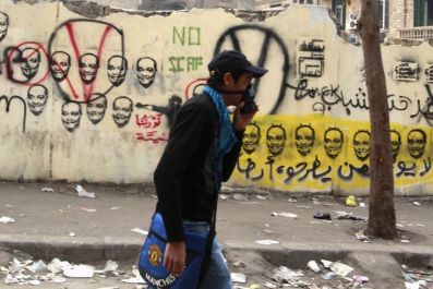 A young man wearing a mask to protect him from tear gas passes a wall with graffiti of Chairman of the ruling Supreme Council of the Armed Forces (SCAF) Mohamed Hussein Tantawi, in the shadow of clashes between police and protesters near the Interior Mini