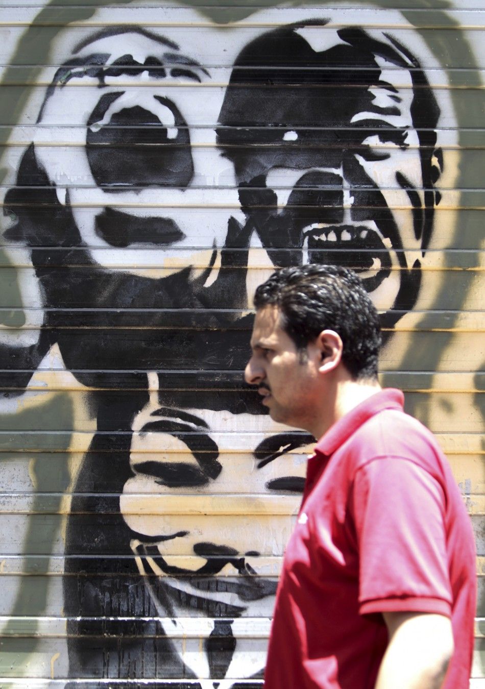 An Egyptian man walks in front of a wall sprayed with graffiti depicting protesters shouting, near Tahrir Square in downtown Cairo