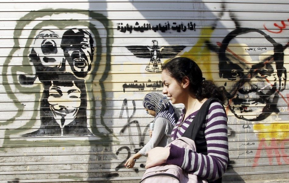 People walk in front of a wall sprayed with graffiti depicting Field Marshal Hussein Tantawi L and martyrs at Mohamed Mahmoud street, which leads to the Interior Ministry, where clashes between protesters and security forces took place during the revolu
