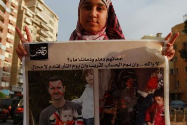 A Syrian refugee girl poses with a placard depicting Syria&#039;s President Bashar al-Assad with his children (L) and children who protesters say were killed by government security forces during a protest in Tripoli, northern Lebanon, May 26, 2012, agains