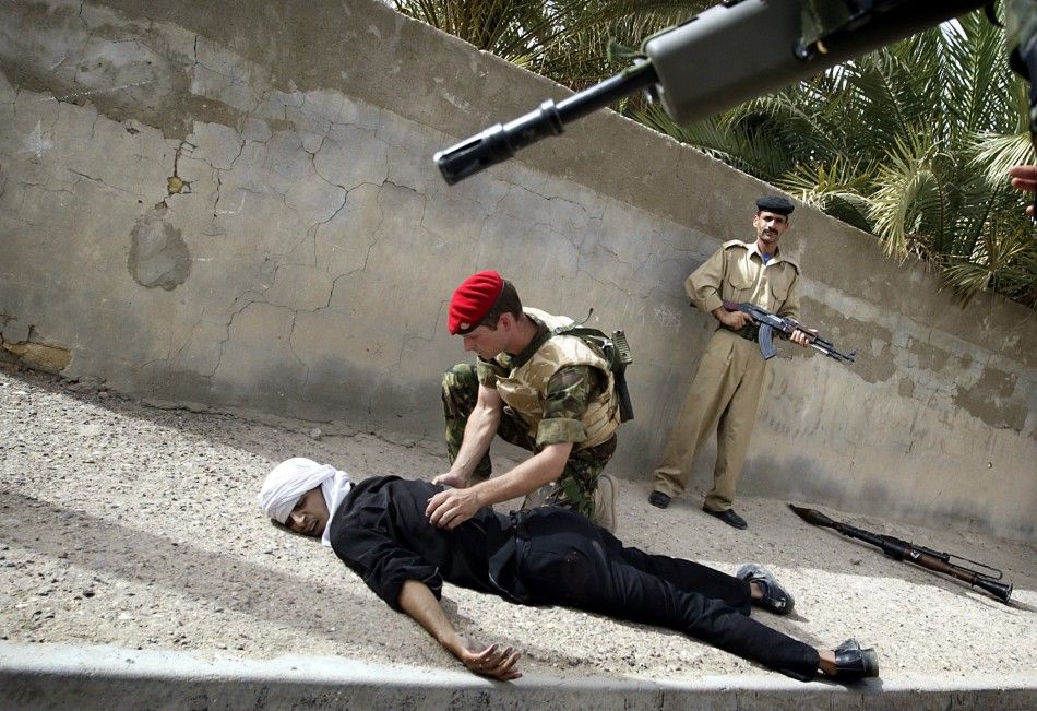 An Iraqi policeman keeps an eye on the crowd as a British military policeman searches a gunman who was shot by coalition soldiers after he threatened a joint police patrol with a rocket launcher in the Hayaniya neighbourhood of Basra May 20, 2003