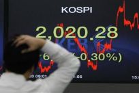 A foreign currency dealer walks past a screen displaying the Korea Composite Stock Price Index (KOSPI) at a bank in Seoul