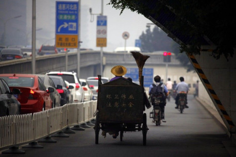 A cleaner rides his tricycle down a side-road as cars sit in a traffic jam along a main road in central Beijing
