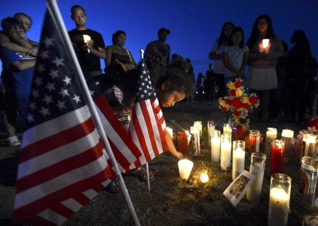 A young boy places a candle by an American flag during a vigil for victims behind a theater where a gunman open fire in Aurora, Colorado