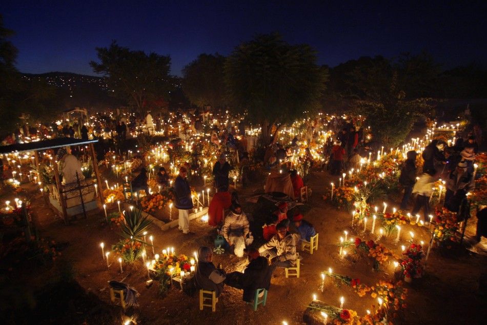 People stand amongst graves decorated with flowers and lit candles at a cemetery in Oaxaca November 1, 2011. Each year, Mexicans celebrate the Day of the Dead by preparing meals and decorating graves of deceased relatives and friends