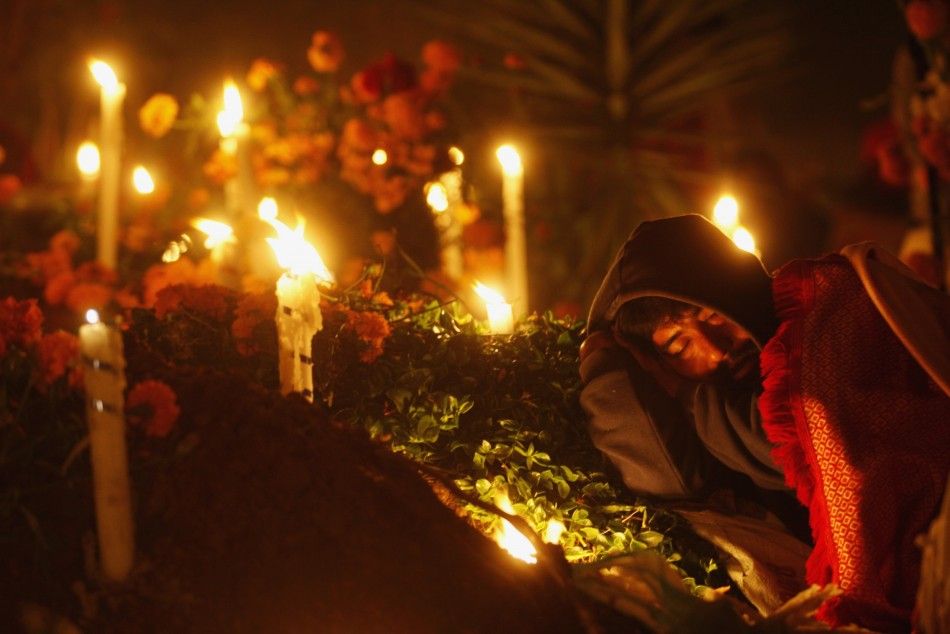 A man sleeps on the grave of a family member decorated with flowers and lit candles at a cemetery in Oaxaca November 1, 2011.