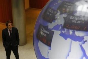 A man stands next to a globe displaying international stock market prices at the London Stock Exchange in the City of London