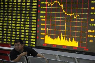 A man sits in front of an electronic board showing stock information at a brokerage house in Huaibei