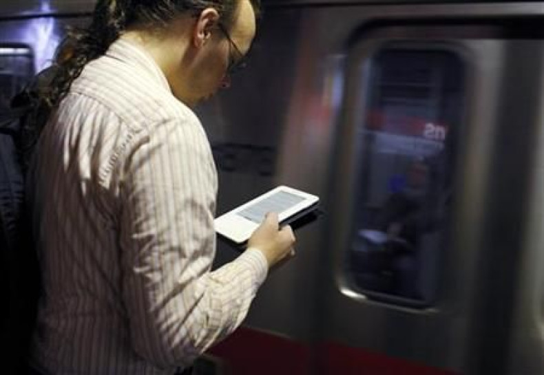 A commuter reads on his Kindle e-reader as a subway train arrives in Cambridge, Massachusetts