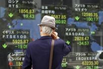 Man looks at an electronic board displaying various market indices from around the world outside a brokerage in Tokyo