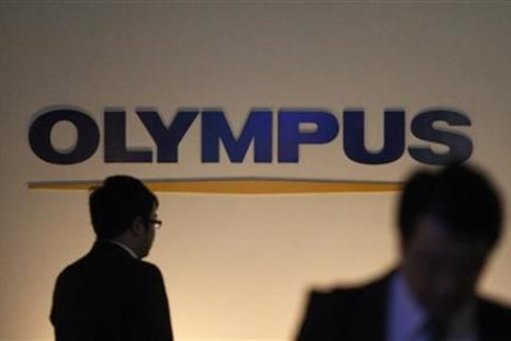 Passersby walk past the company logo of Olympus Corp. in Tokyo