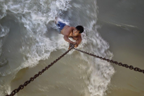 A man clings to chains suspended from a bridge as he bathes in rapidly flowing waters of the Ganges river in Haridwar