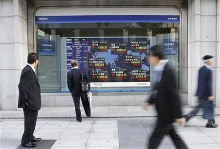 Passersby look at an electronic board displaying a rise in major market indices around the world, outside a brokerage in Tokyo