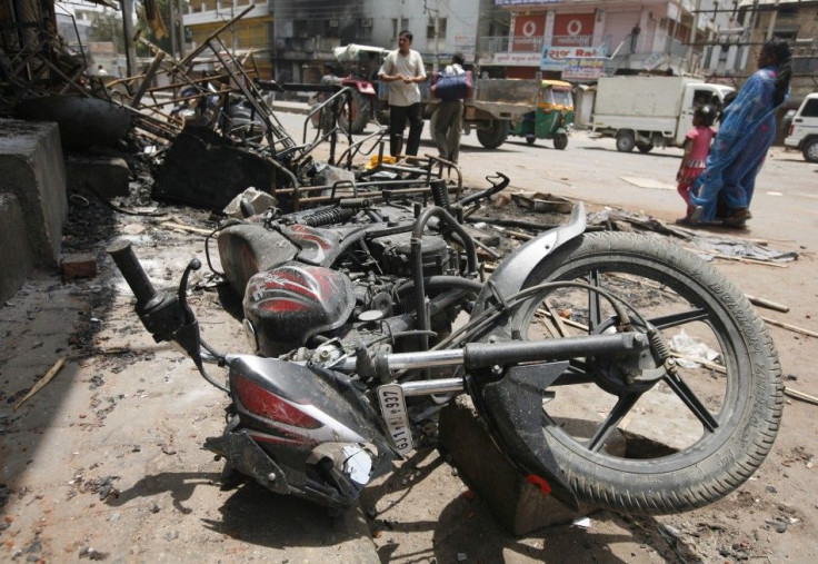 Commuters walk past debris of burnt vehicles after a clash between two communities at Sanand