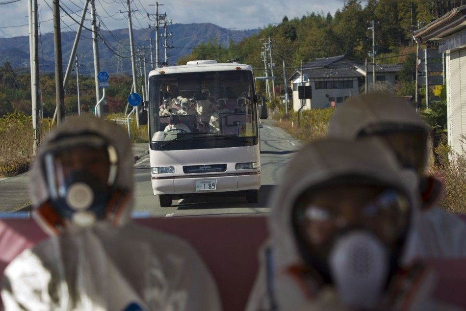 Japanese officials wearing protective suits and masks ride in the back of a bus