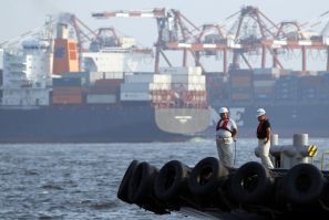 Workers stand on a ship in front of cargo ships at a port in Tokyo