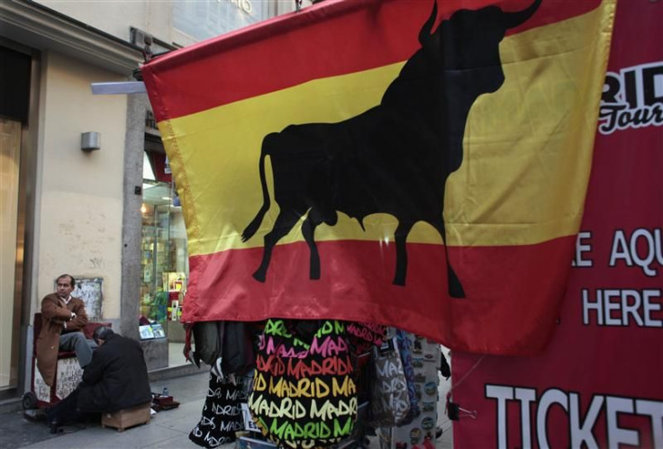 A man gets a shoeshine next to a kiosk displaying a Spanish flag with a bull on it in downtown Madrid