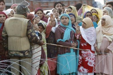 A security personnel directs with a baton at the relatives of Kashmiri Hajj pilgrims, to not cross the barbed wires before the pilgrims&#039; departure in Srinagar
