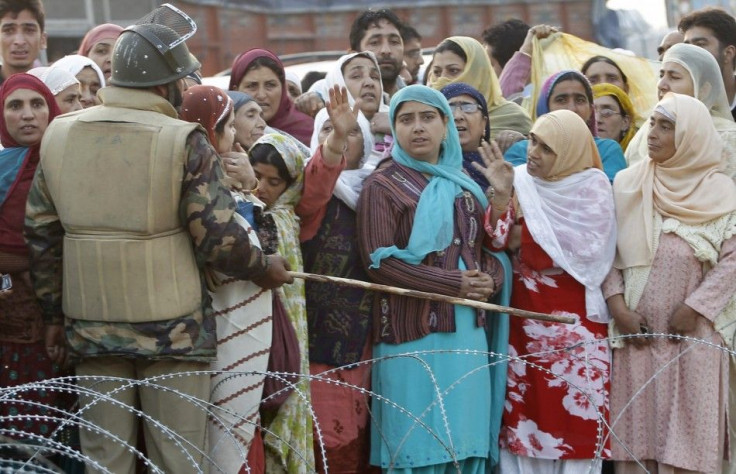 A security personnel directs with a baton at the relatives of Kashmiri Hajj pilgrims, to not cross the barbed wires before the pilgrims&#039; departure in Srinagar