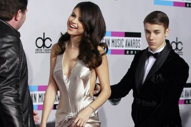 Singer Justin Bieber carries the train of his girlfriend, singer Selena Gomez' dress, as they arrive at the 2011 American Music Awards in Los Angeles