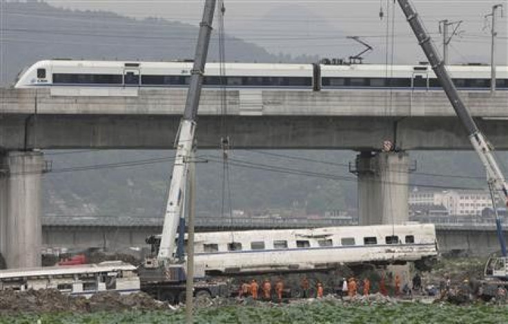 A high speed bullet train runs past a railway bridge as workers use cranes to lift a wrecked carriage