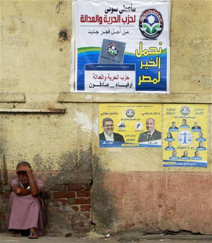 A beggar sits beside posters for parliamentary elections by Egypt&#039;s Muslim Brotherhood &quot;The Freedom and Justice Party&#039;&quot; in Cairo