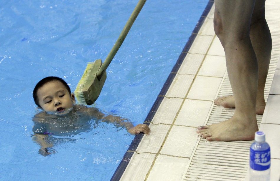 Coach holding broom tries to prevent boy from holding onto edge of pool during a diving training session at a training centre in Beijing