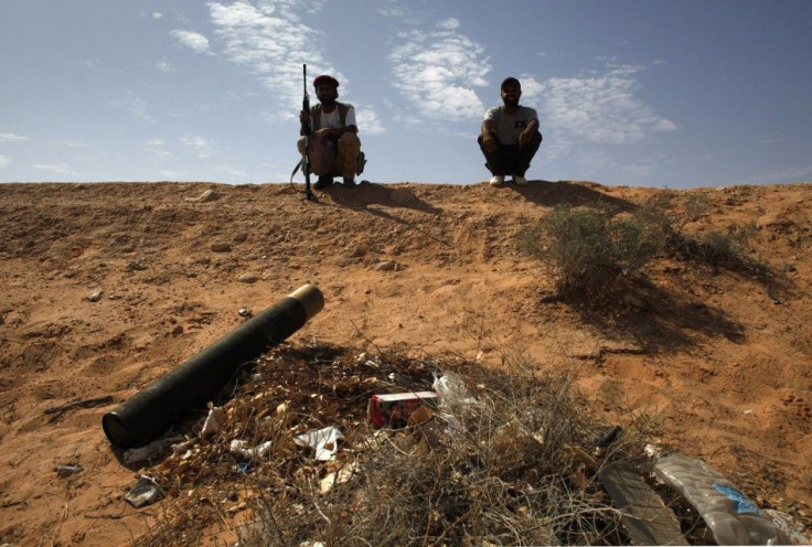 Libyan rebel fighters sit on a ridge near a tank shell after overrunning a government army position in the village of Hawamid