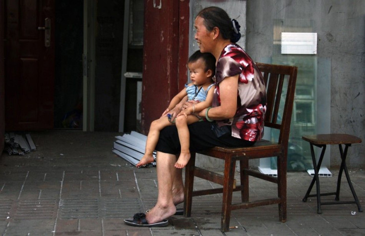 A woman sits on a chair with her grandchild along a main road in Beijing