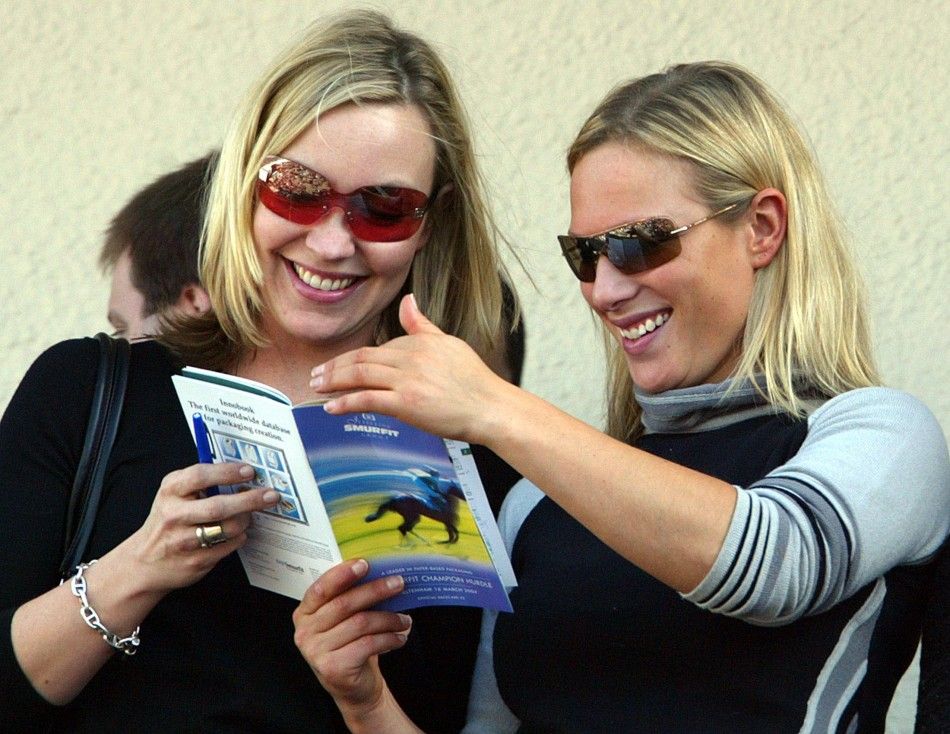 Britains Zara Phillips R studies the race card with an unidentified friend before the first race at the Cheltenham National Hunt Festival meeting in southern England