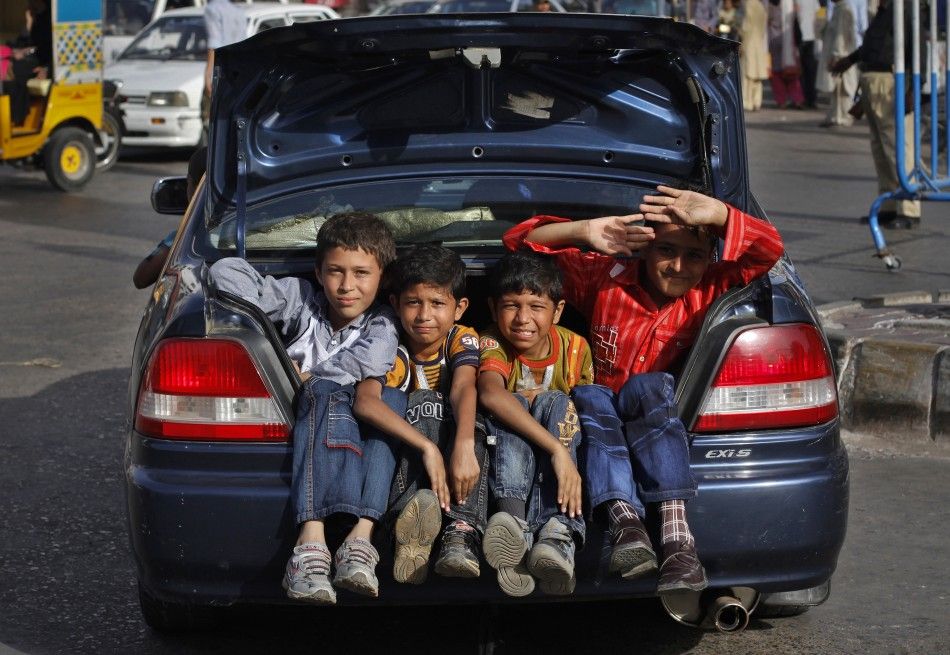 Boys sit in the trunk of a car while travelling on a street in Karachi
