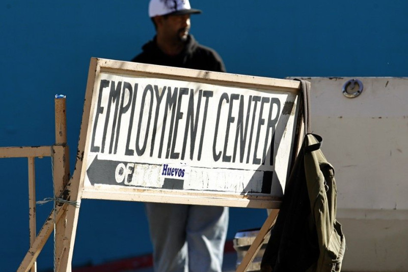 A day labourer stands behind a sign for an employment center in San Diego