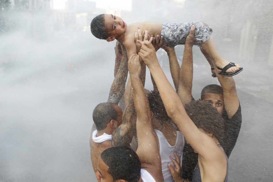 A group of men lift a child into the stream of an open fire hydrant in the Brooklyn borough of New York