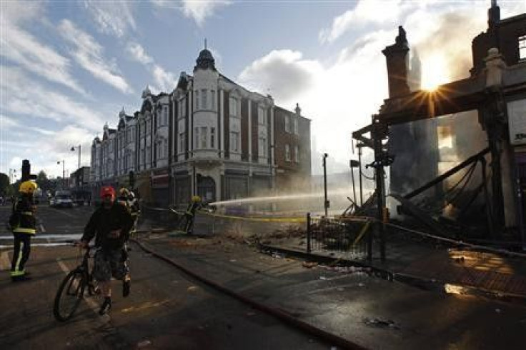 A cyclist passes firemen dowsing down buildings set alight during riots in Tottenham, north London