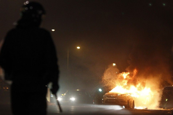 A police officer wearing riot gear stands near a burning police car in Tottenham