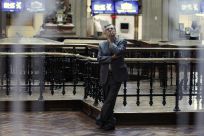 A trader is seen through a window as he looks at screens at the bourse in Madrid
