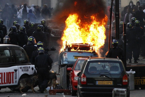 Police officers in riot gear block a road near a burning car on a street in Hackney, east London August 8, 2011