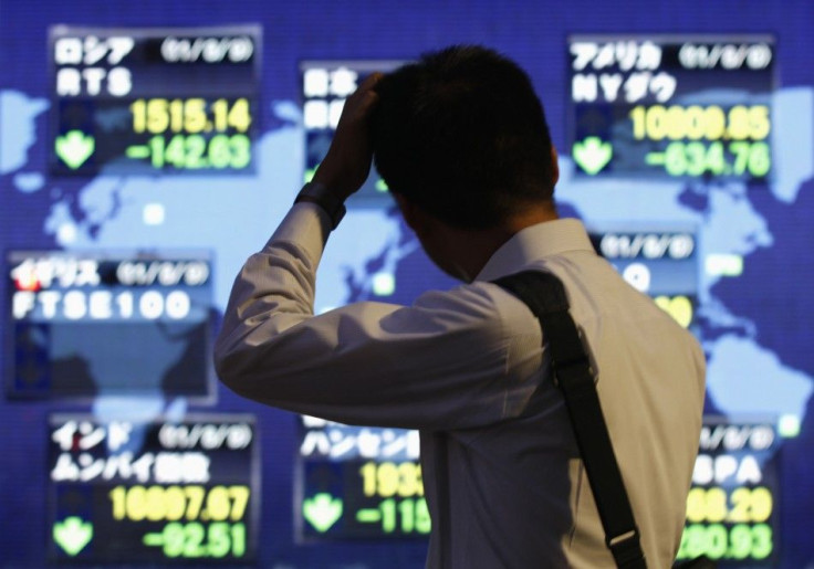 A man scratches his head in front of an electronic board displaying falls in major market indices around the world, outside a brokerage in Tokyo