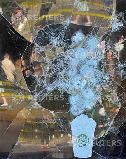Pedestrians are reflected in the broken window of a coffee shop in Ealing in west London