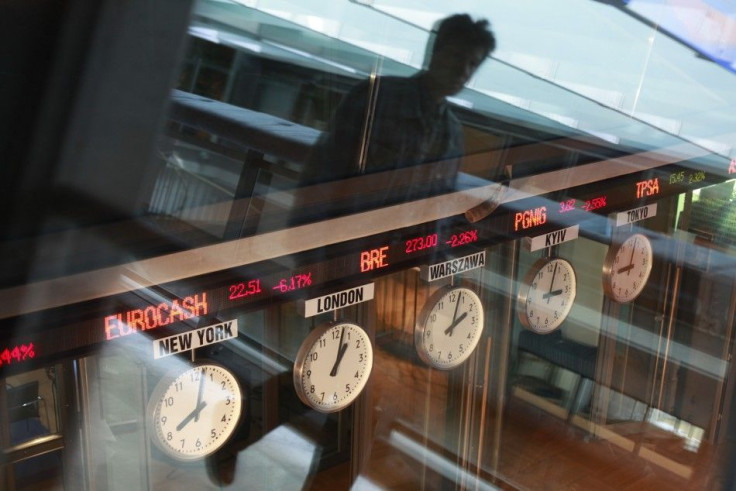 A man reflects in a window as he passes near clocks at the Warsaw Stock Exchange