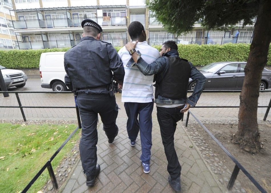 Police officers lead away a man following a raid on a property in Pimlico London August 11, 2011.