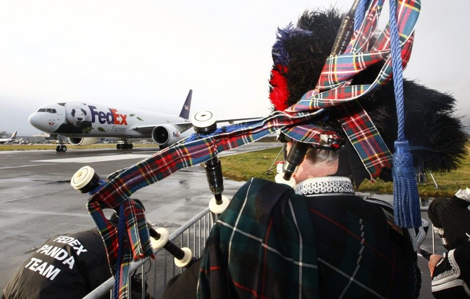 A bagpiper watches as the FedEx Panda Express aircraft carrying two giant pandas taxis along the runway at Edinburgh airport in Scotland