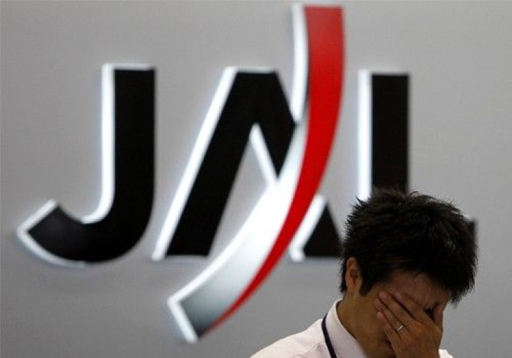 A worker reacts in front of a logo of Japan Airlines (JAL) at its check-in counter at Haneda airport in Tokyo